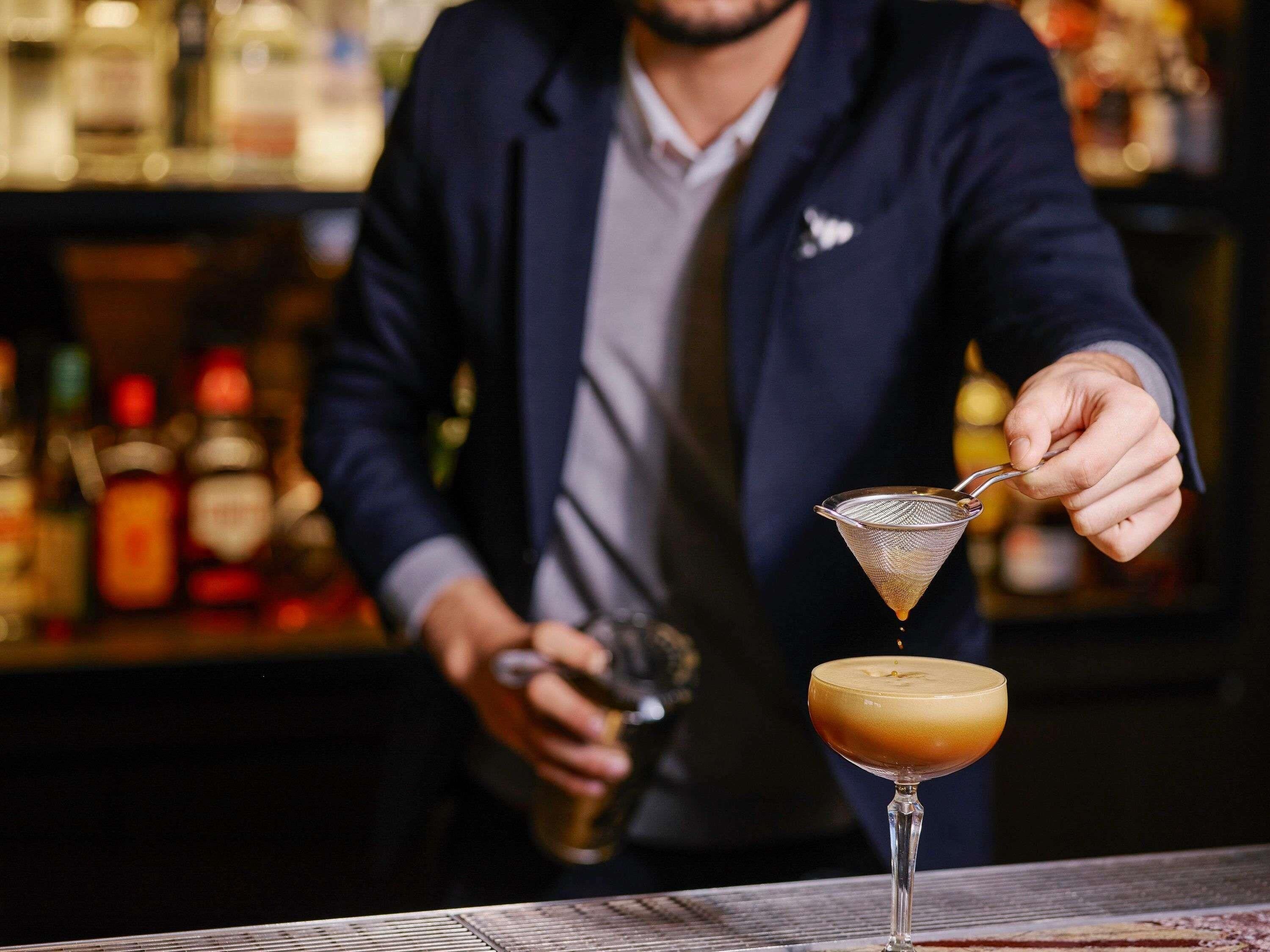 A bartender preparing a cocktail with a strainer.