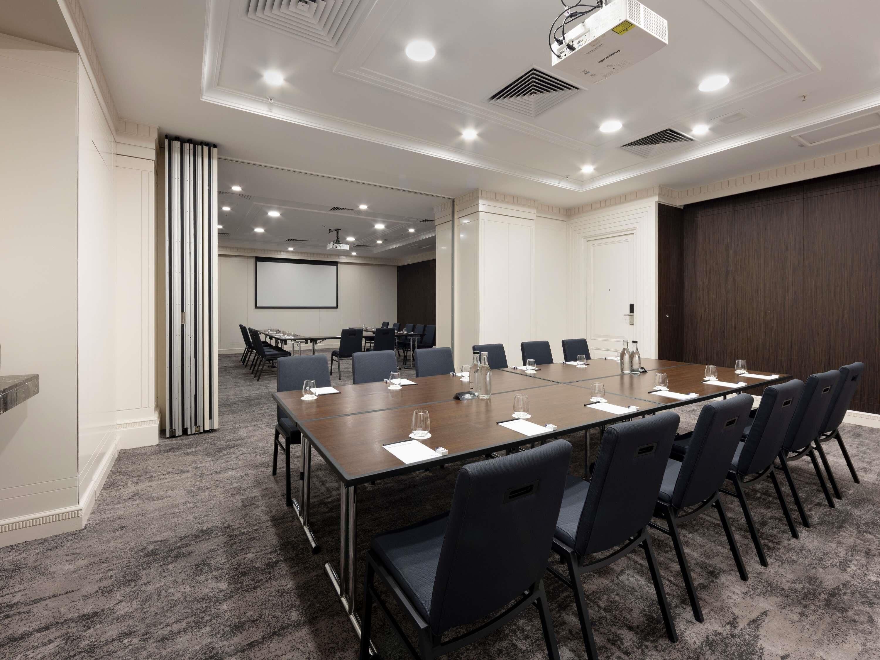 A conference room with a long table, chairs, a projector, and a screen.