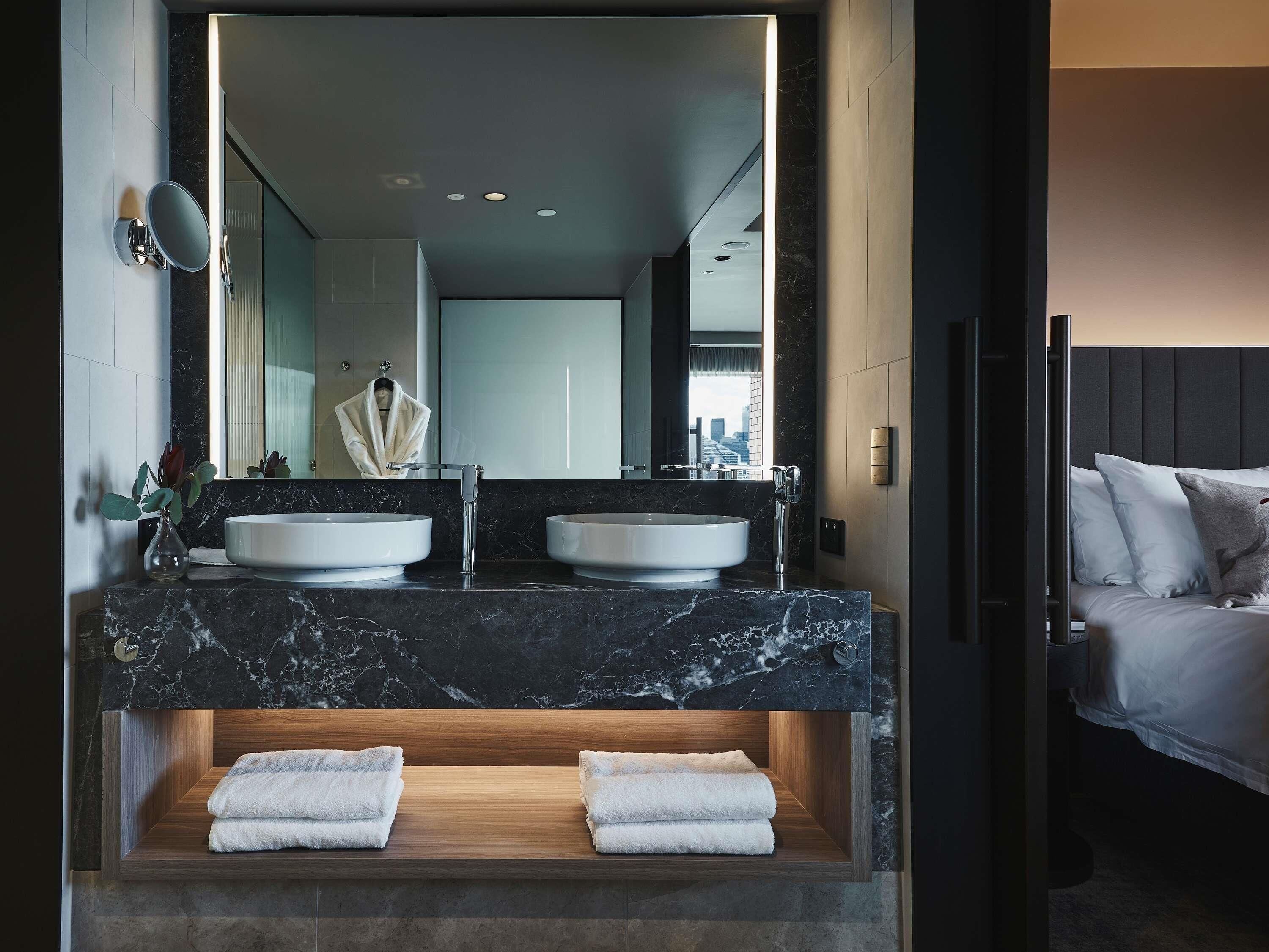 A modern bathroom with two sinks, a large mirror, and a wooden vanity with towels.