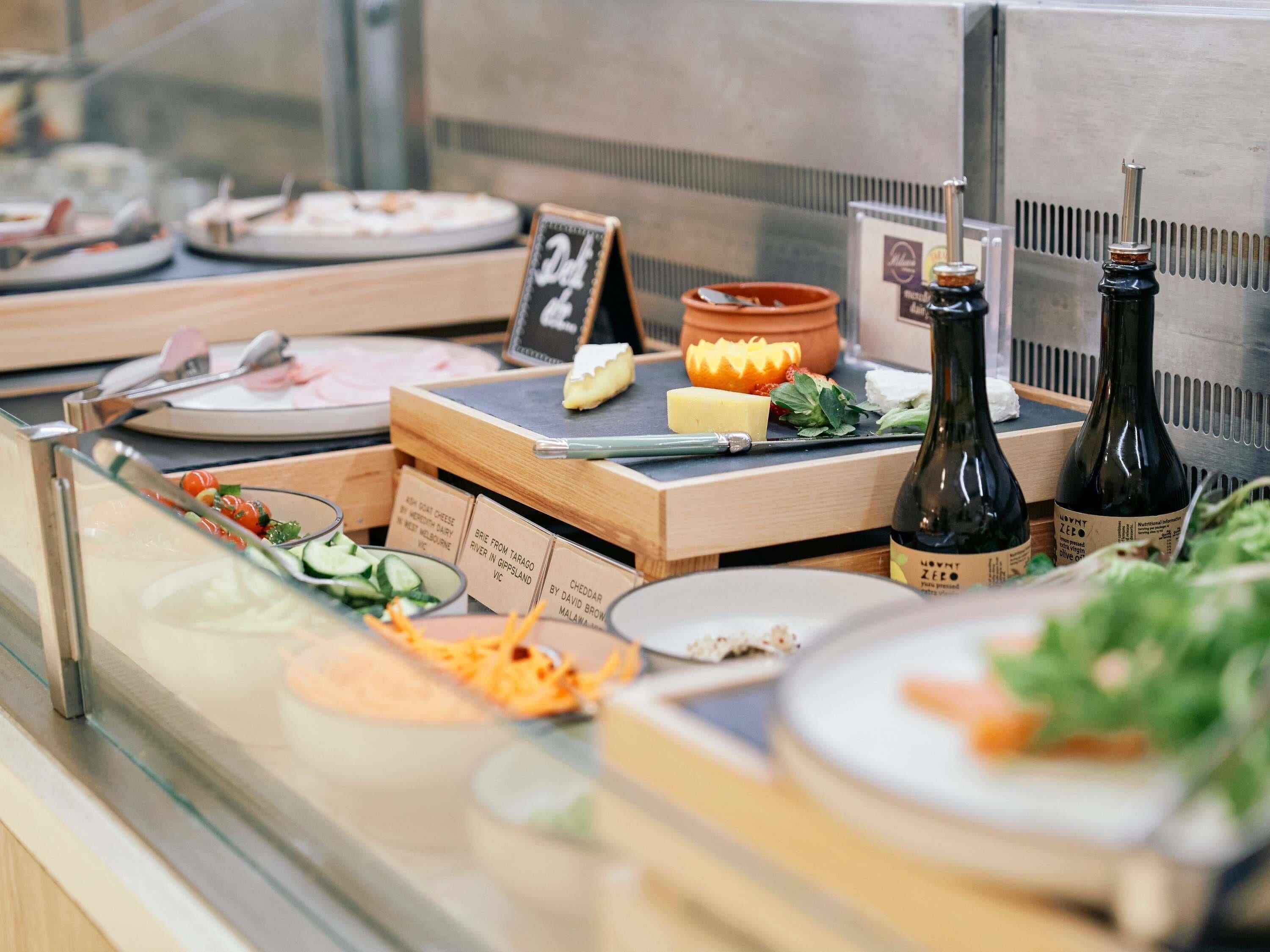 A food display with various cheeses, a chalkboard menu, and bottles of wine.
