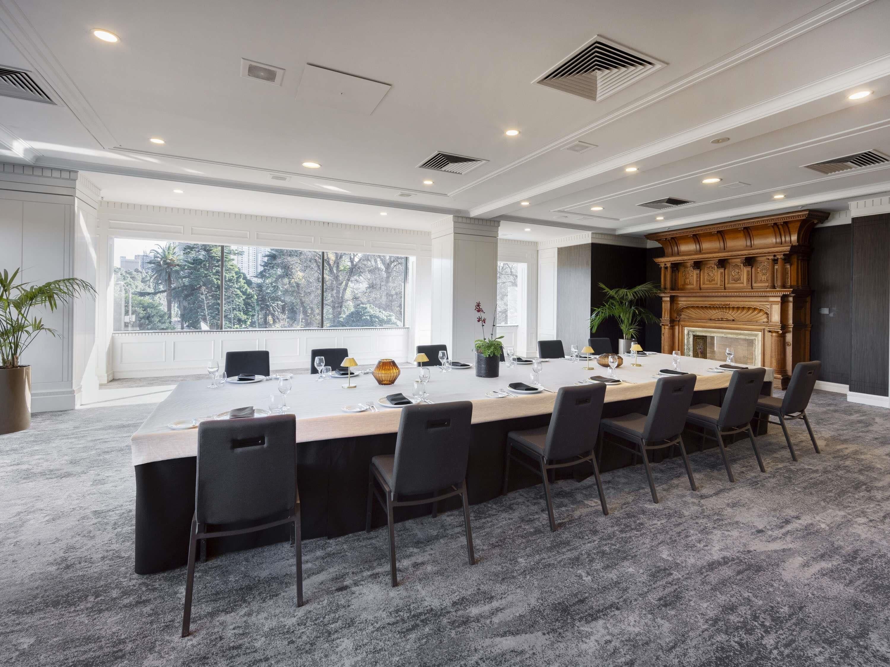 Uma sala de conferências com uma mesa comprida, cadeiras, lareira e janelas amplas.