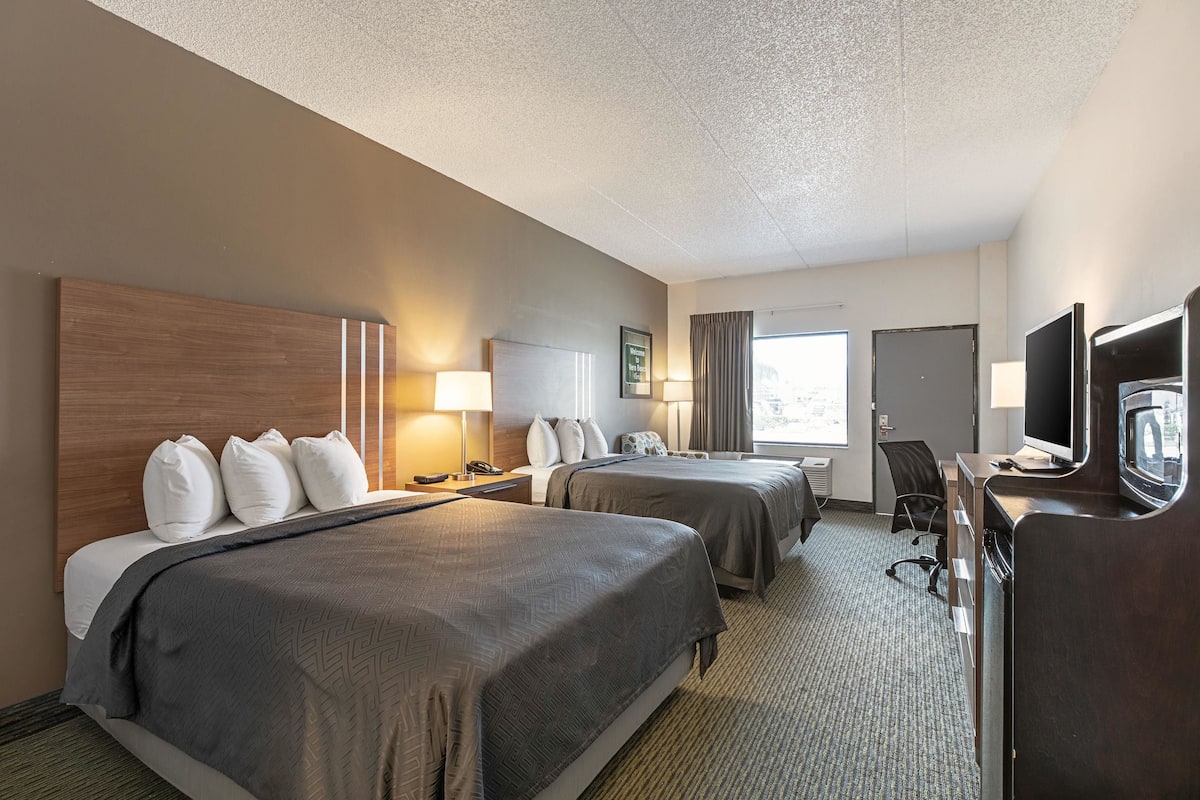 A hotel room with two beds, a desk with a computer, a TV, and a window with curtains.