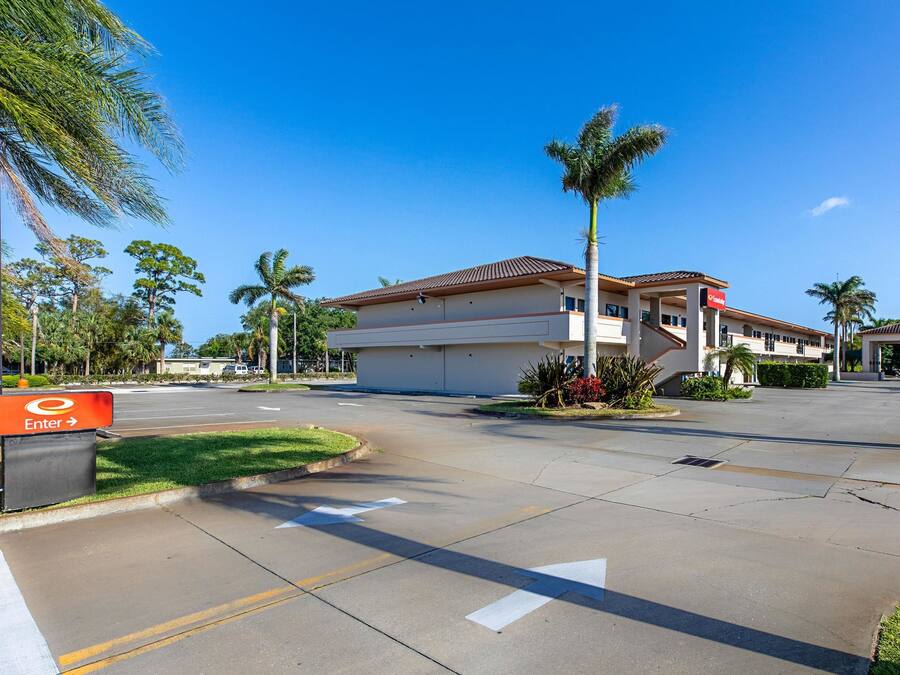 A hotel entrance with a clear driveway, palm trees, and a sign indicating an entrance.