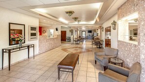 A spacious lobby with a marble wall, a reception desk, seating area, and a clock on the wall.