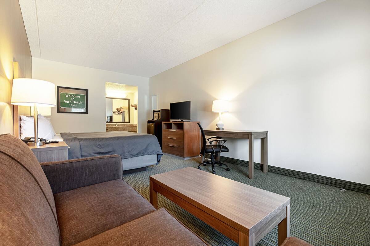 A hotel room with a bed, a desk, a chair, a sofa, and a lamp.