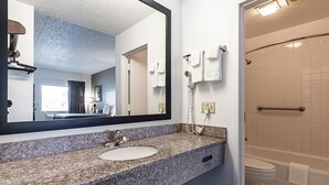 A modern bathroom with a granite countertop, a sink, a mirror, a towel rack, a hairdryer, and a bathtub.