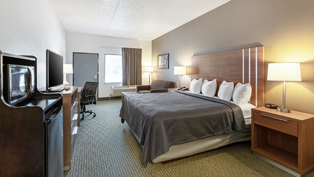 A hotel room with a bed, bedside lamps, a desk with a computer, a television, and a window with curtains.