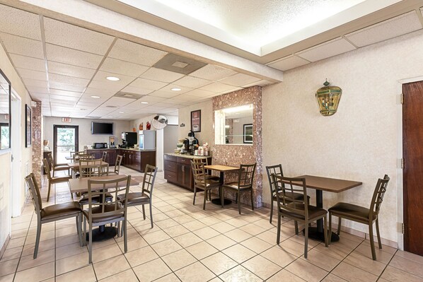 A spacious dining area with multiple tables and chairs, a kitchen in the background, and a decorative wall lamp.