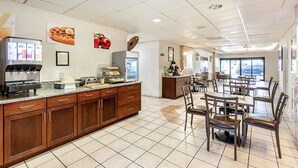 A spacious kitchen area with a coffee machine, toaster, and food display. There are wooden cabinets and a tiled floor.