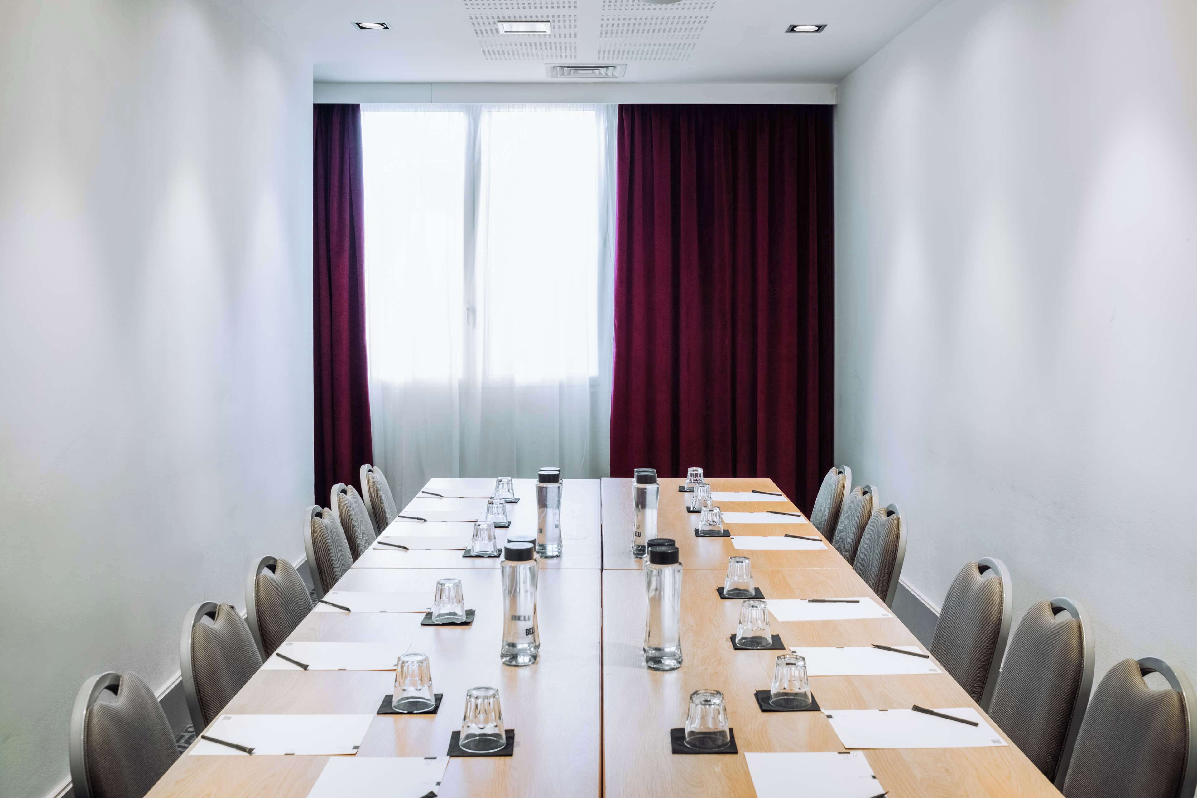 Un salón de conferencias con una larga mesa, sillas y botellas de agua.