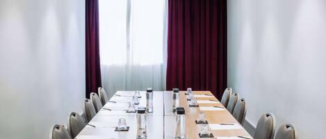 Un salón de conferencias con una larga mesa, sillas y botellas de agua.