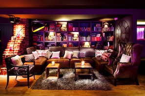 A cozy living room with a leather sofa, two side tables, a bookshelf, and a fireplace. - pentahotel Reading (Reading)