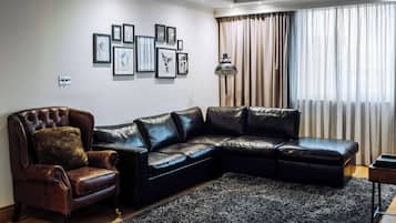 A living room with a leather sofa, a leather armchair, a black rug, and framed artwork on the wall.