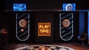 A dartboard with a neon sign that reads "PLAY TIME" in the center of a room with a checkered floor pattern. - pentahotel Reading (Reading)