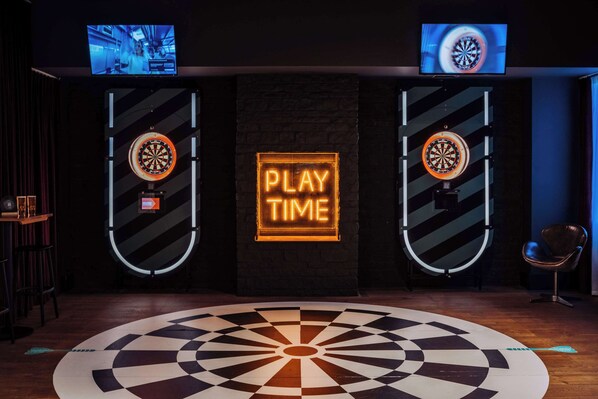 A dartboard with a neon sign that reads "PLAY TIME" in the center of a room with a checkered floor pattern.