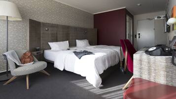 A modern hotel room with a large bed, a desk, a chair, and a lamp.