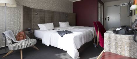 A modern hotel room with a large bed, a desk, a chair, and a lamp.
