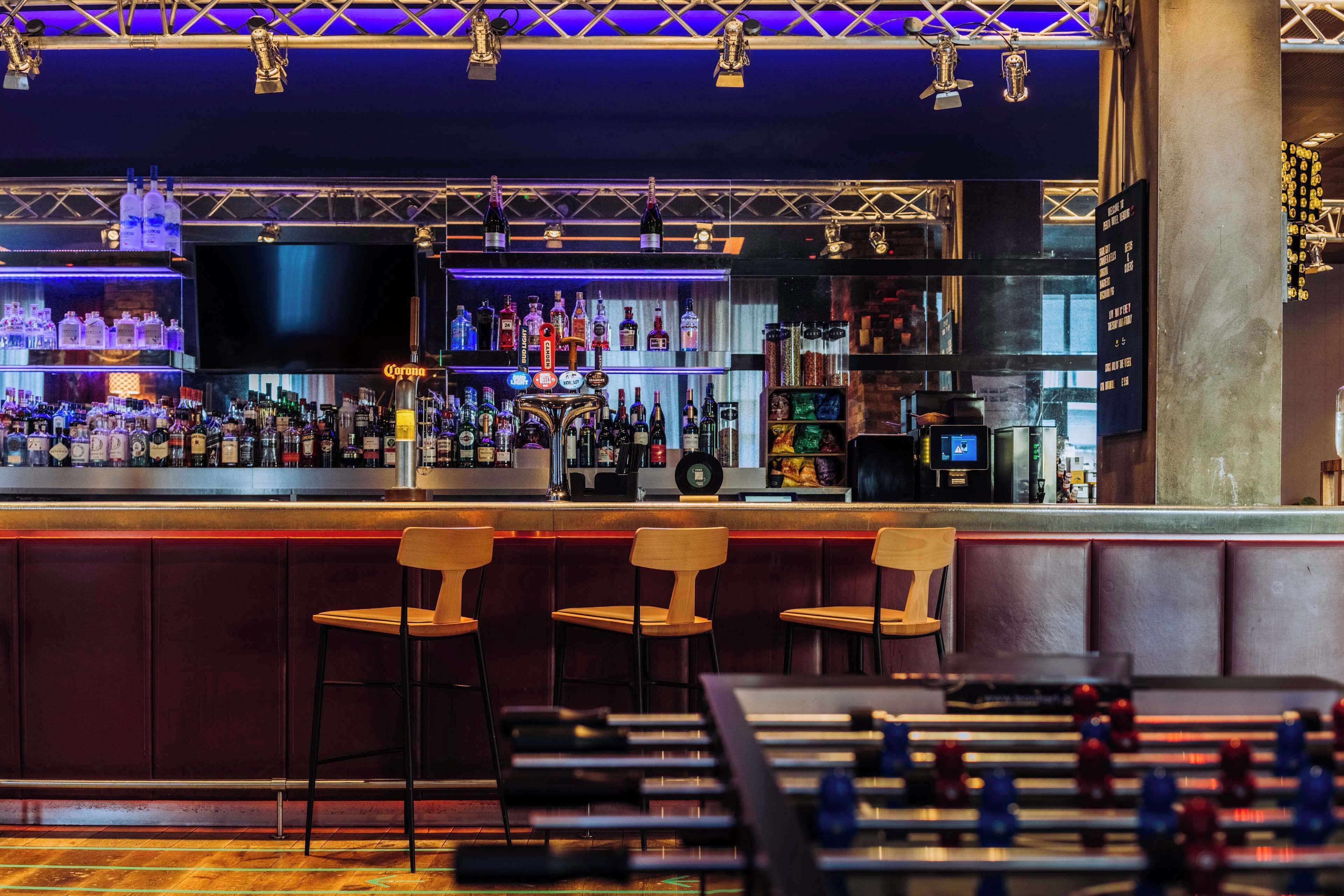 A bar area with stools, a foosball table, and a variety of liquor bottles.