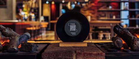Un code QR sur un objet circulaire noir, avec les inscriptions « GOOD FOOD » et « DRINKS MENU », dans un décor intérieur moderne.
