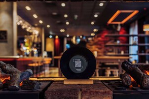 Un code QR sur un objet circulaire noir, avec les inscriptions « GOOD FOOD » et « DRINKS MENU », dans un décor intérieur moderne.