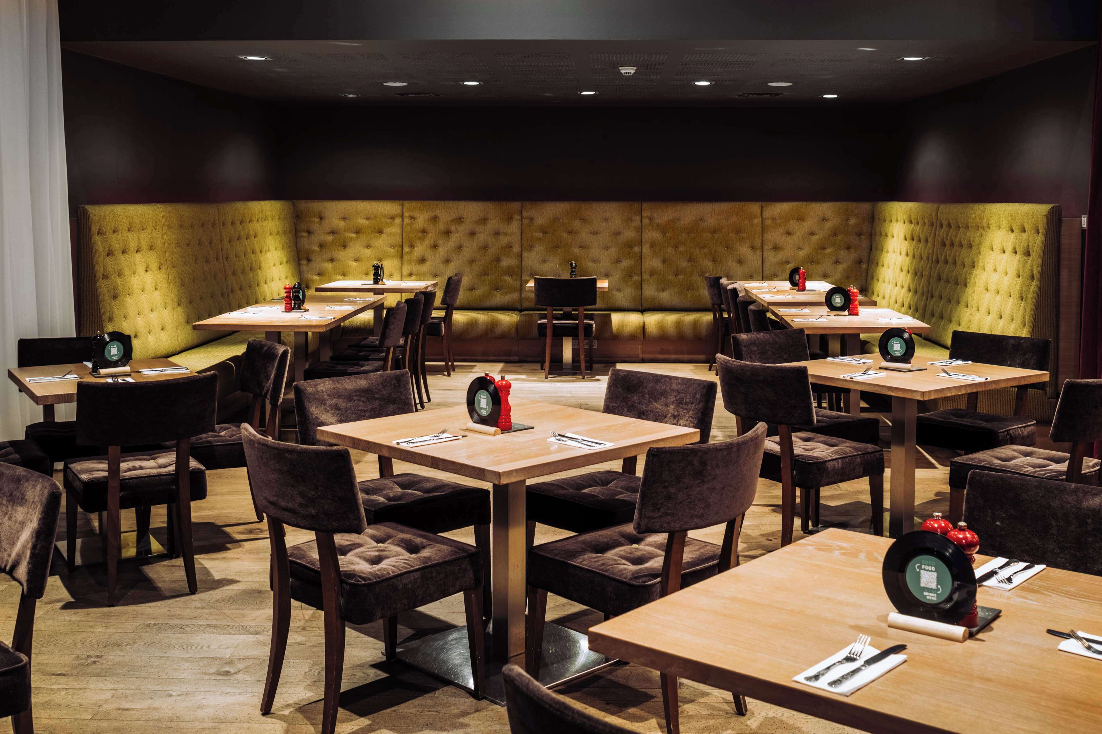 A restaurant with booths and tables, each set with cutlery and a red decorative item.
