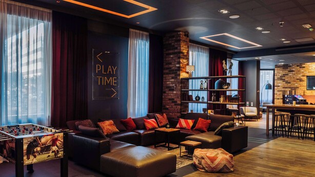 A modern lounge area with a foosball table, leather sofas, a bookshelf, and a bar area. - pentahotel Reading (Reading)