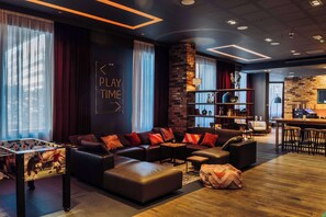 A modern lounge area with a foosball table, leather sofas, a bookshelf, and a bar area.
