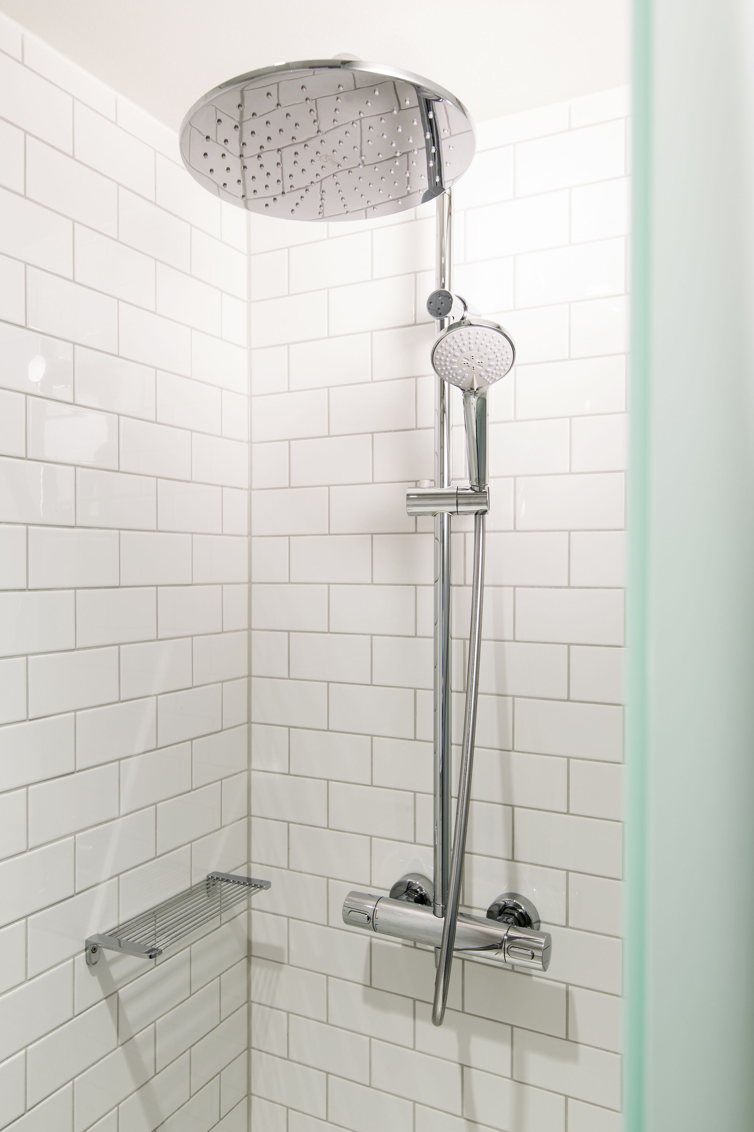 Ducha con cabezal de ducha de mano y ducha lluvia, montada en una pared con azulejos blancos.
