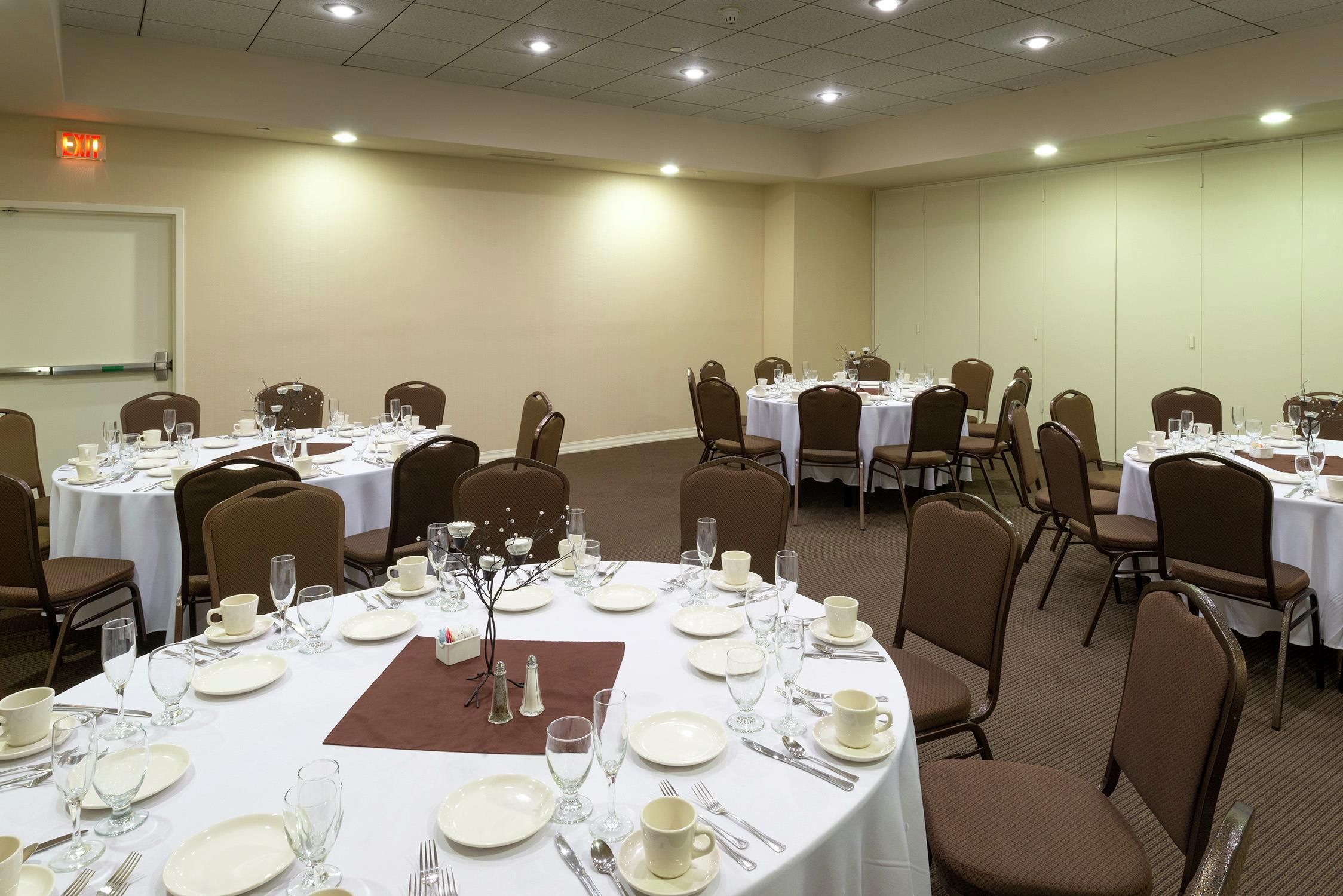 A conference room with multiple round tables set for dining, equipped with chairs and table settings.