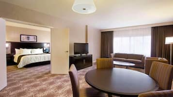 A hotel room with a bed, a TV, a sofa, a dining table, and a chair.