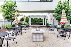 An outdoor patio area with a fire feature, multiple tables and chairs, and striped umbrellas. - DoubleTree by Hilton Hotel Binghamton (Binghamton)