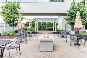 An outdoor patio area with a fire feature, multiple tables and chairs, and striped umbrellas.
