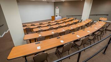 A conference room with multiple rows of tables and chairs, a podium, and an exit sign.