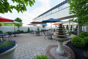 An outdoor patio area with tables and chairs, umbrellas, and a central water feature. - DoubleTree by Hilton Hotel Binghamton (Binghamton)