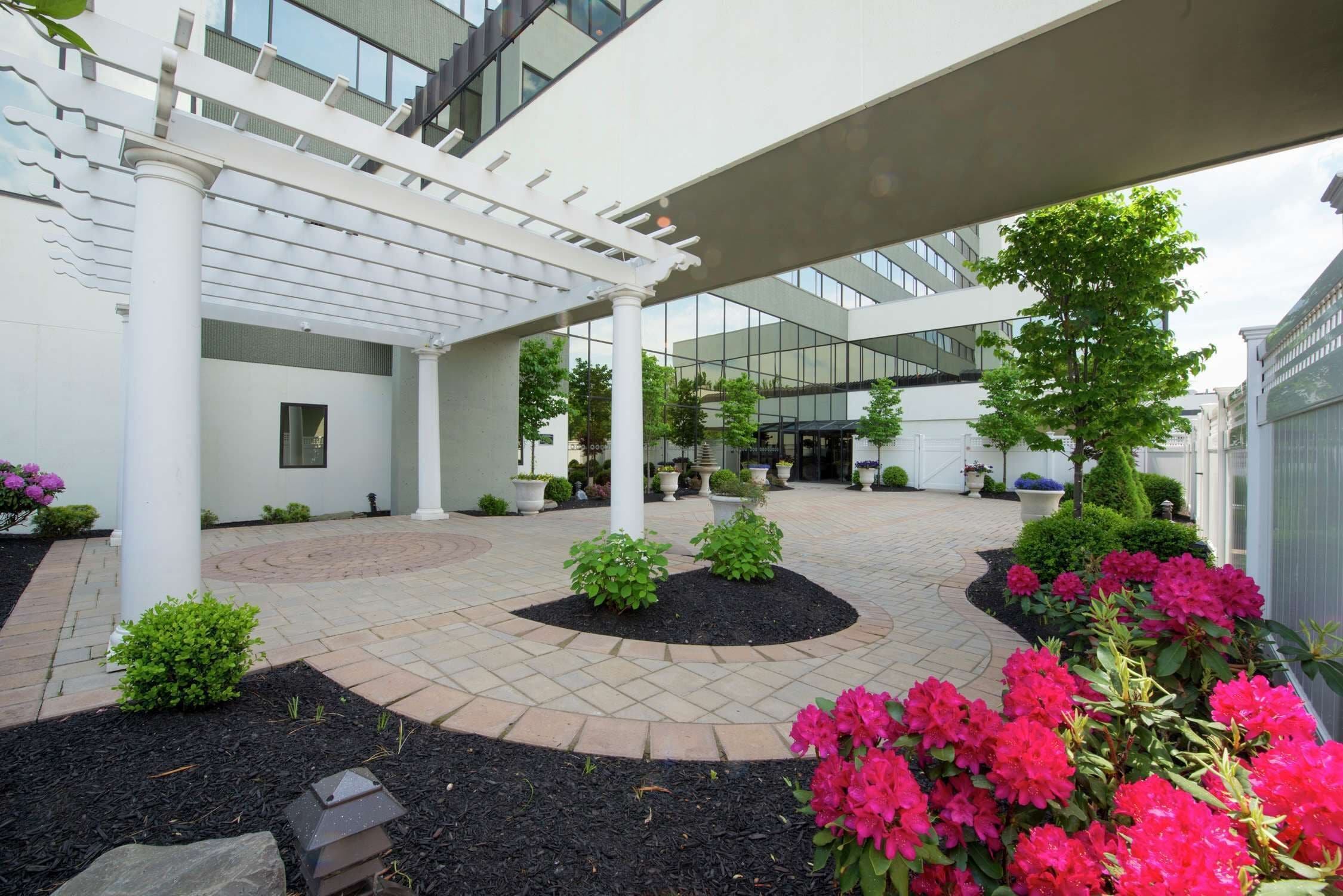 A modern building with a covered walkway, potted plants, and a landscaped garden area.