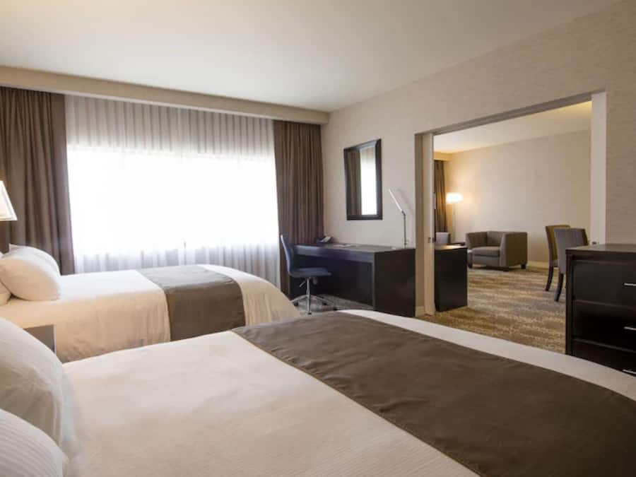 Camera d'albergo con due letti, una scrivania, una sedia, una televisione e un'ampia finestra con tende.