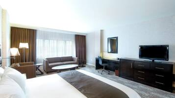 A hotel room with a bed, a sofa, a desk, a chair, a television, and a window with curtains.