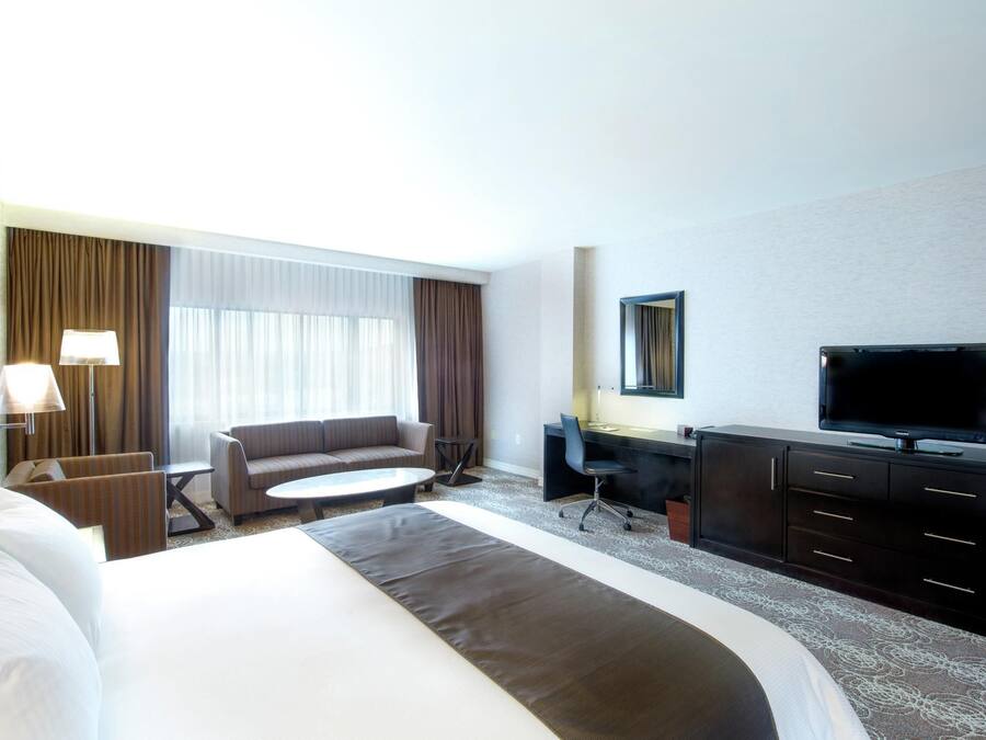 A hotel room with a bed, a sofa, a desk, a chair, a television, and a window with curtains.