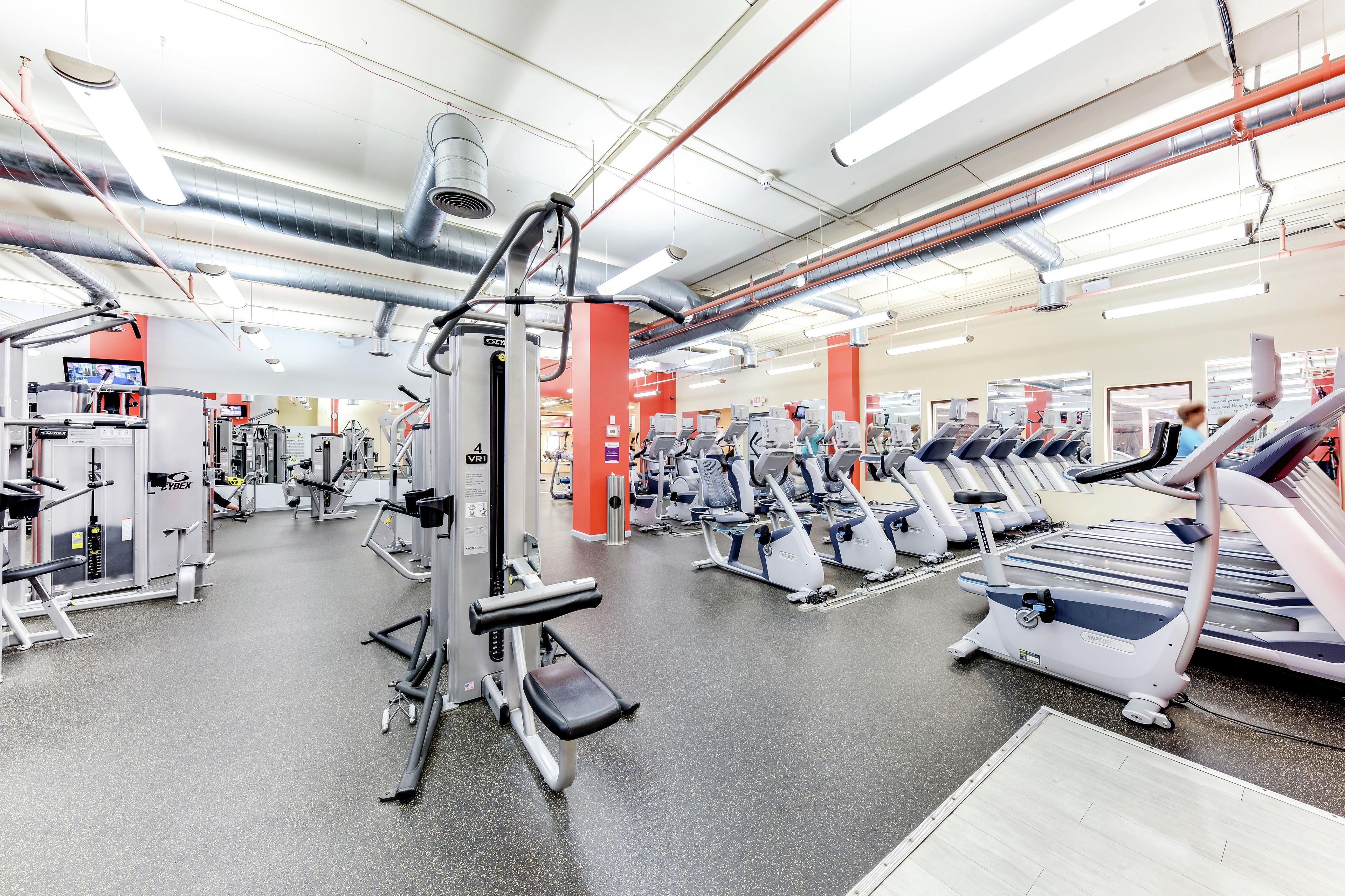 Un gimnasio con diversos equipos de ejercicio, incluyendo cintas de correr y máquinas de pesas.