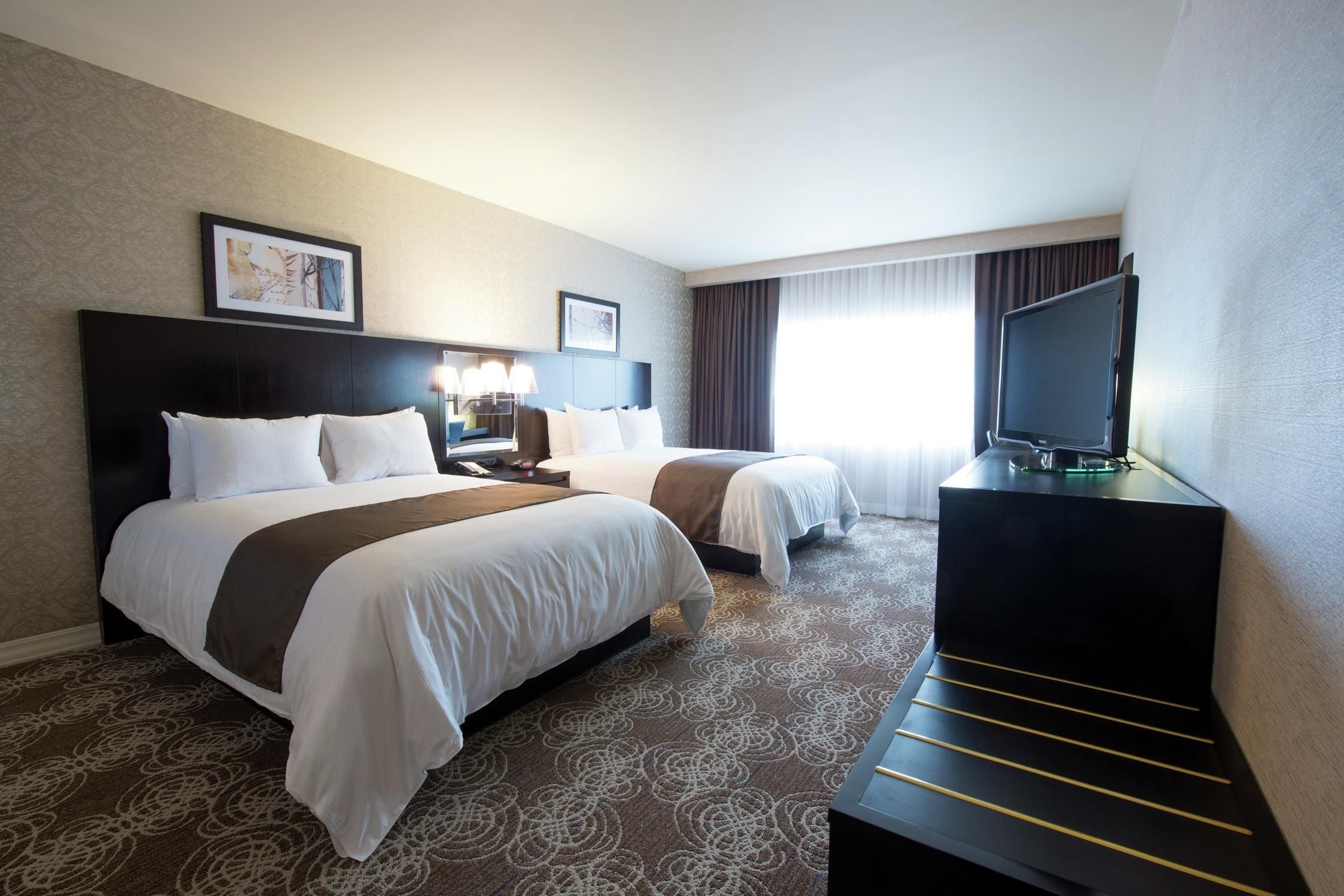 A hotel room with two beds, a TV, and a desk.
