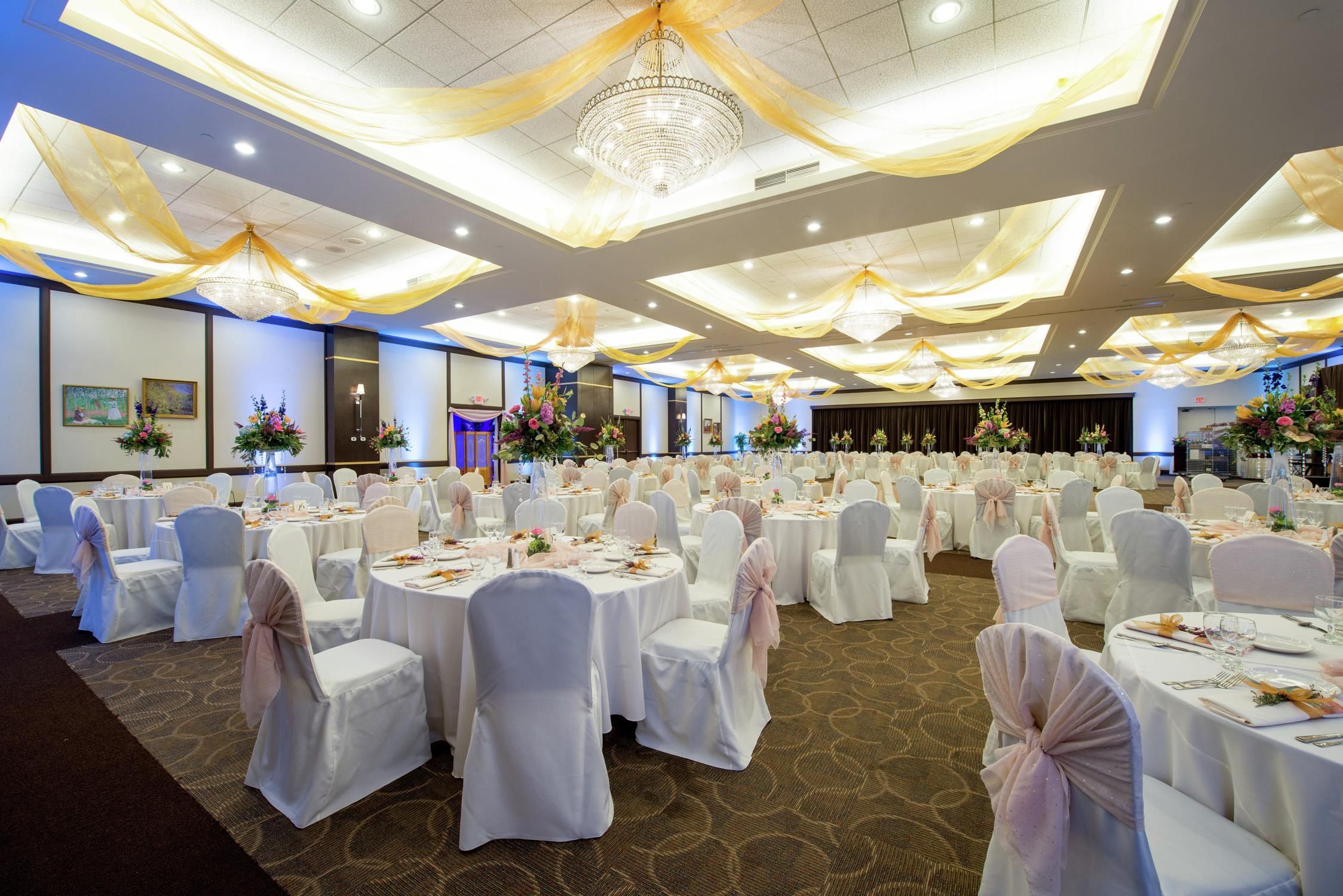 A banquet hall with round tables, white chairs, and chandeliers.