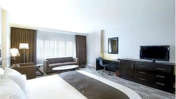 A hotel room with a large bed, a sofa, a desk, a TV, and a window with curtains.