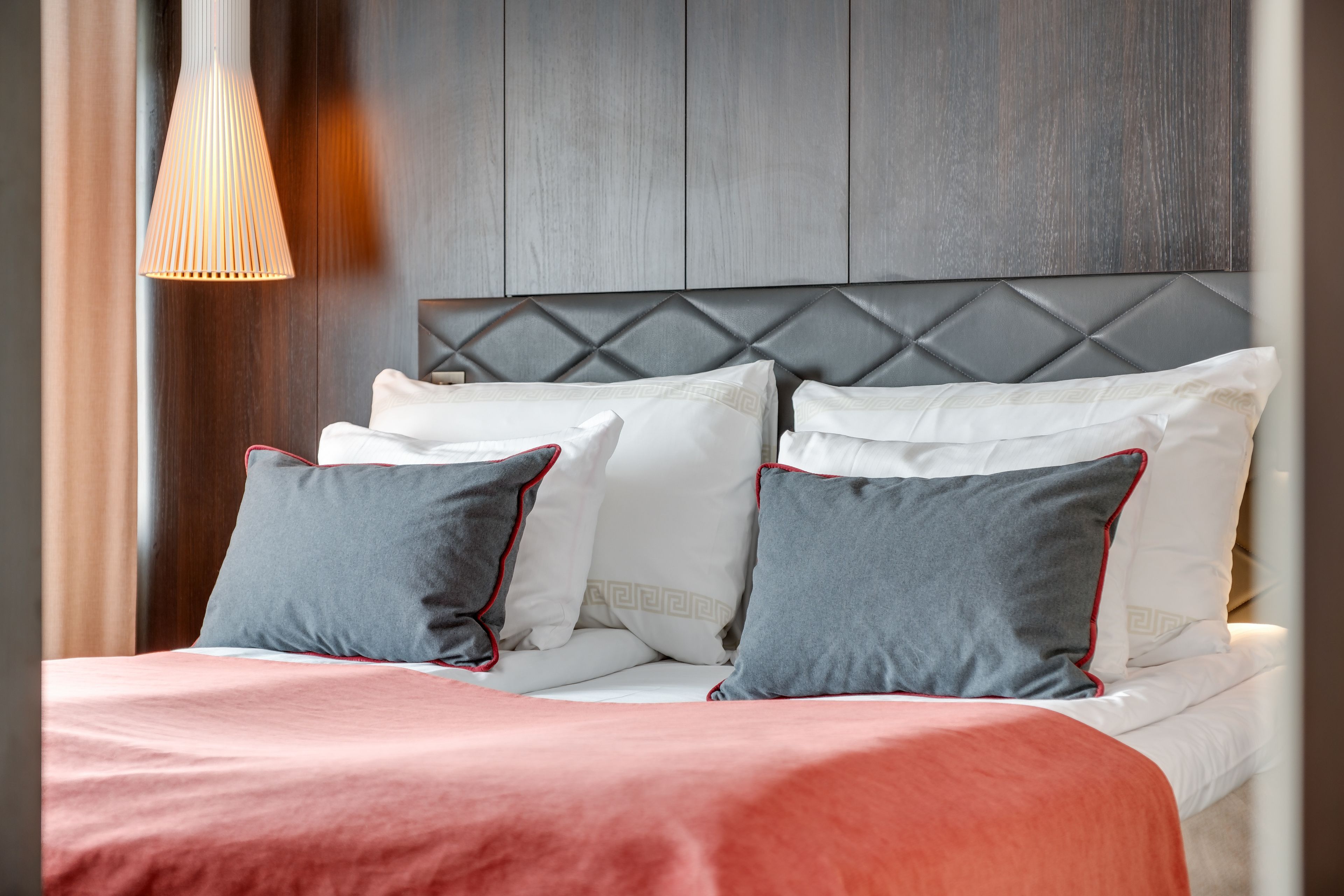 A neatly made bed with a red and white bedspread, grey and white pillows, and a wooden headboard.
