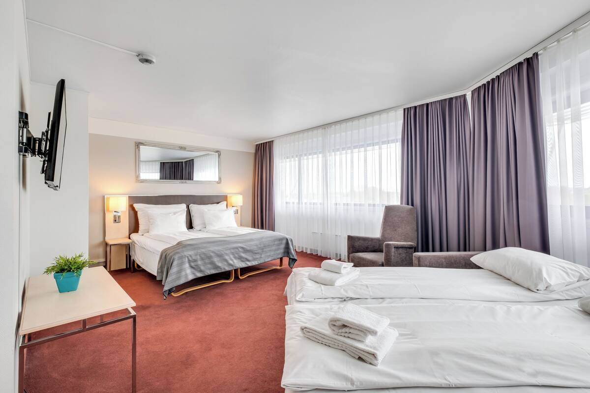 Habitación de hotel con dos camas, un escritorio, una silla, un ventanal con cortinas y un espejo en la pared.