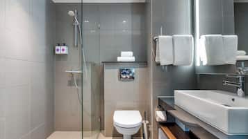 Um banheiro moderno com box de vidro, vaso sanitário branco, pia com espelho e toalhas brancas dobradas.