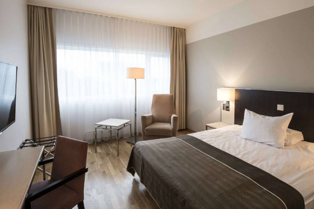 Una habitación de hotel con cama, escritorio, silla, televisor y lámpara.