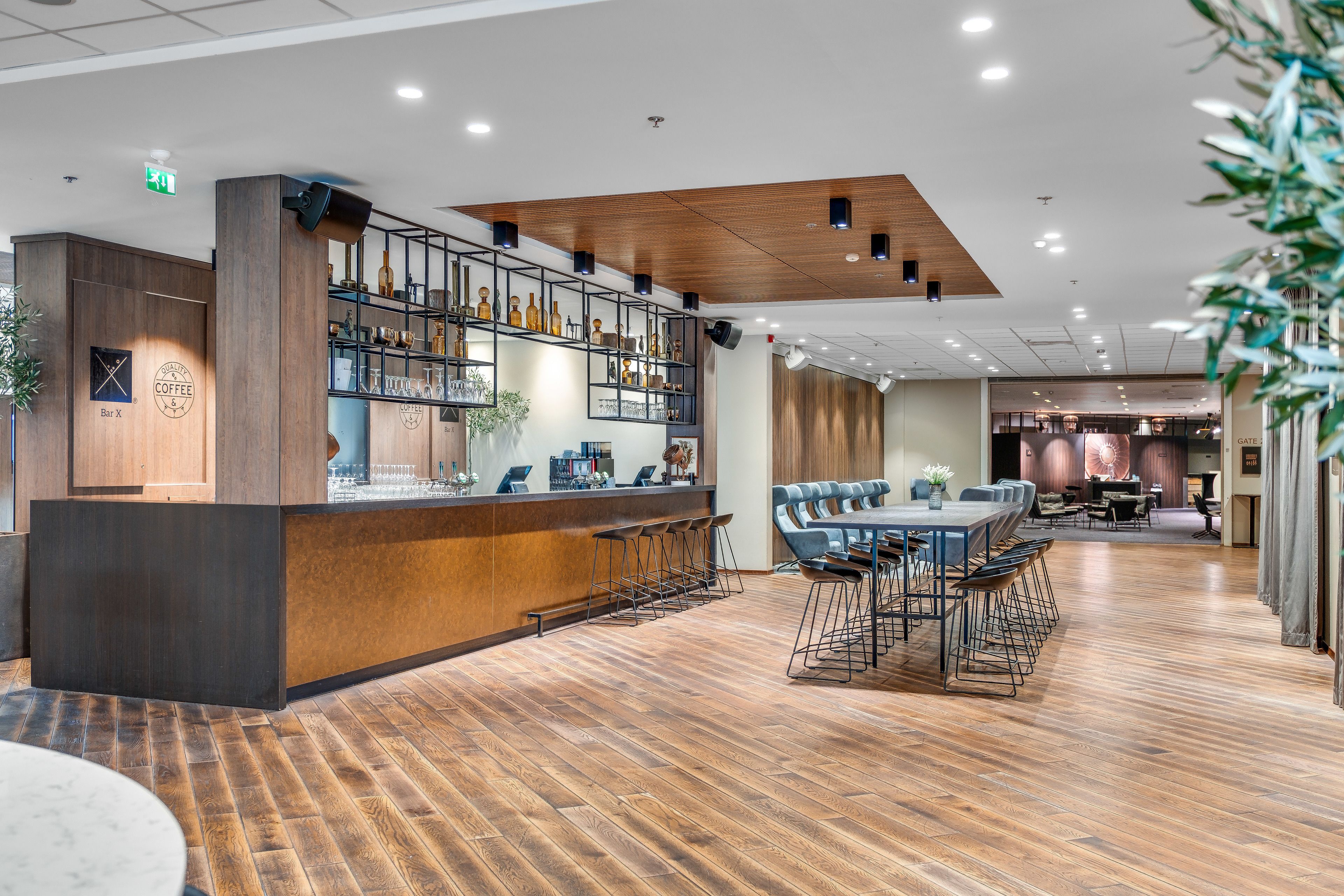 A modern bar area with wooden flooring, a long counter with stools, and a variety of bottles and glasses on shelves.