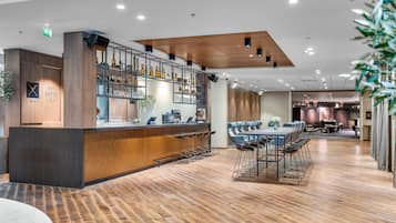 A modern bar area with wooden flooring, a long counter with stools, and a variety of bottles and glasses on shelves.