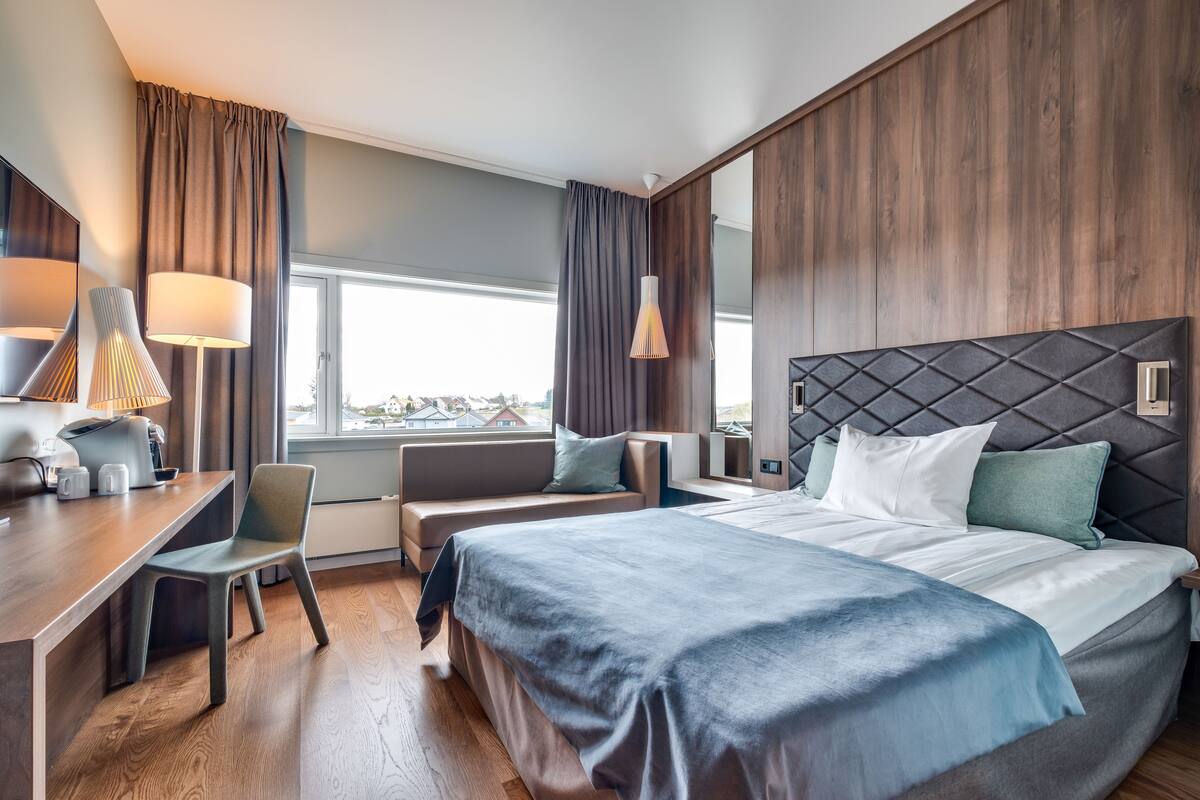 Una habitación de hotel moderna con una cama grande, un escritorio, una silla y una ventana con cortinas.