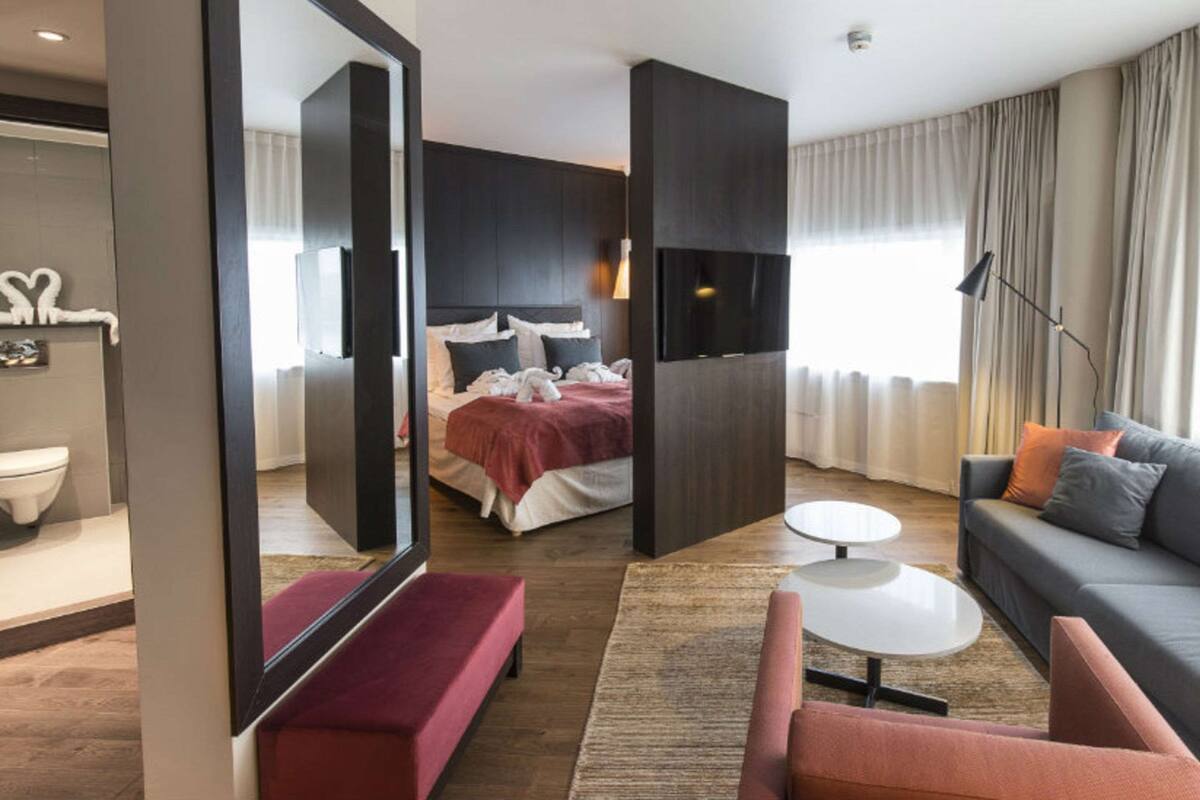 Una habitación de hotel moderna con cama, sofá, una mesita y un espejo.